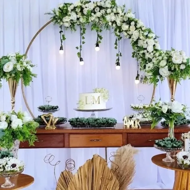 Mesa do bolo de casamento com arco floral e arranjos